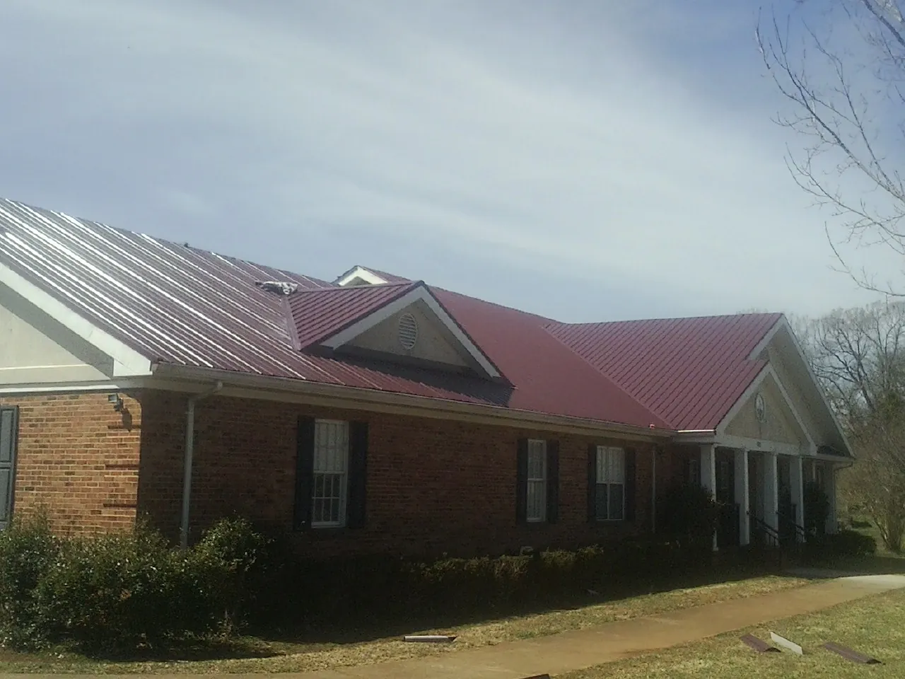 Red metal roof with gabled entries on a long brick building, from a Hail Damage Roof Repair job in Frederick