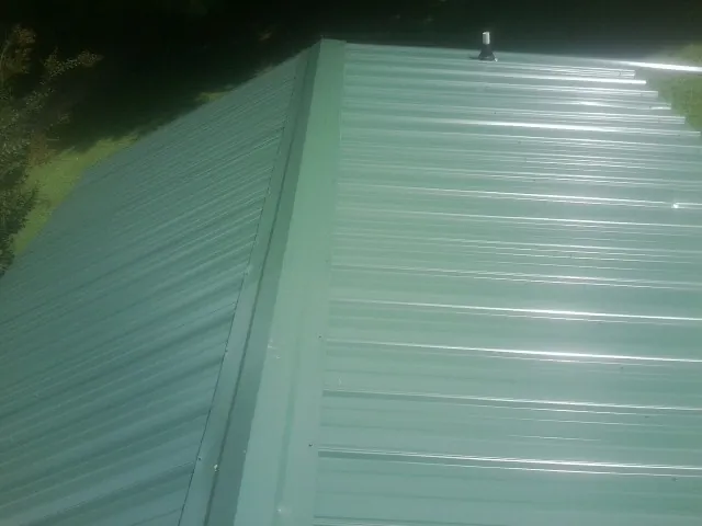 New green metal panels meeting at the ridge of a roof — Flat Roof Repair work by our crew in Frederick