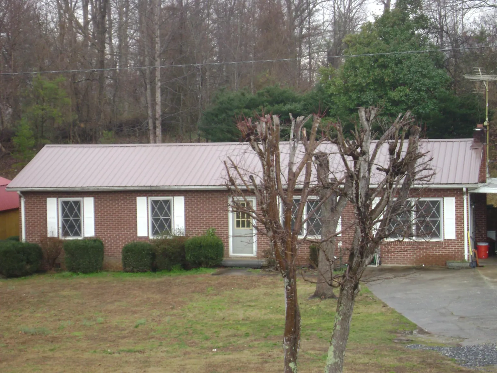 Mauve metal roof on a brick ranch home behind bare trees in Frederick